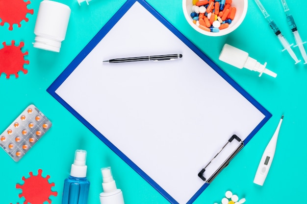 Top view paper holder with pen, bacteria, thermometer sprays and pills on cyan blue background. horizontal