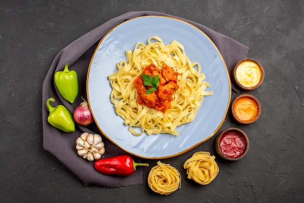 Top view pasta bowls of sauces pasta colorful ball pepper garlic onion next to the appetizing pasta with meat and herbs on the tablecloth