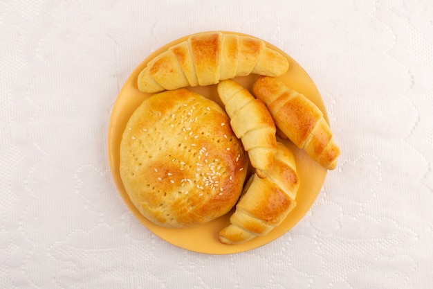 top view pastries along with croissants inside orange plate on the white floor