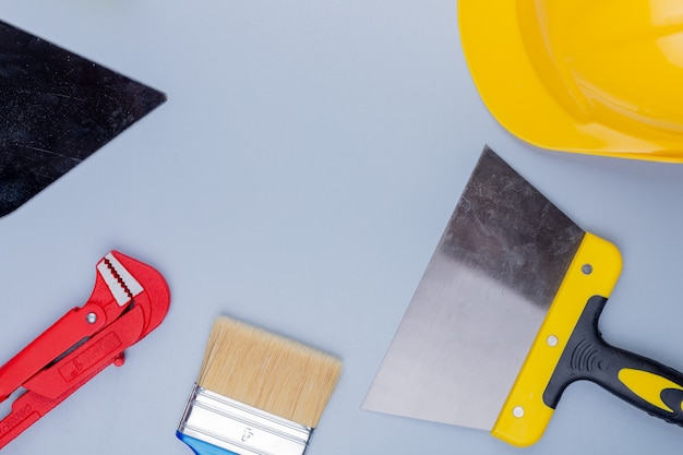 Top view of pattern from set of construction tools as pipe wrench safety helmet trowel paint brush and putty knife on gray background