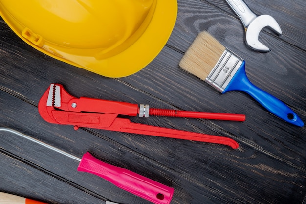 Free photo top view of pattern from set of construction tools as screwdriver pipe wrench safety helmet paint brush and open-end wrench on wooden background