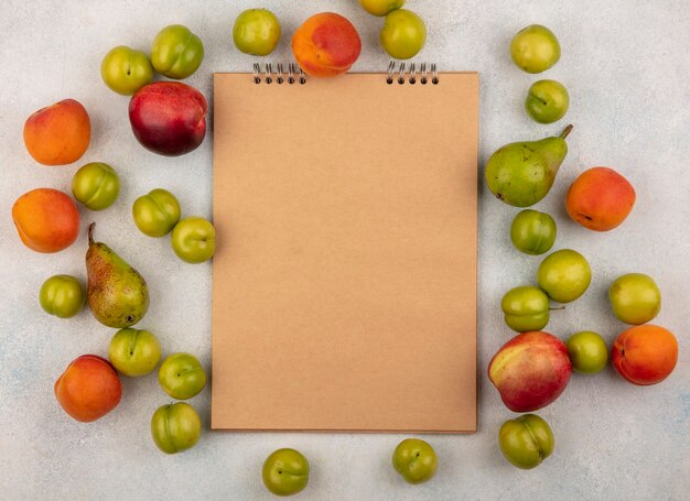 Free photo top view of pattern of fruits as plum peach and pear around note pad on white background with copy space