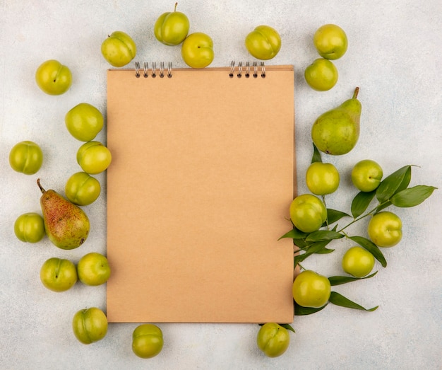 Free photo top view of pattern of fruits as plum and pear with leaves around note pad on white background with copy space