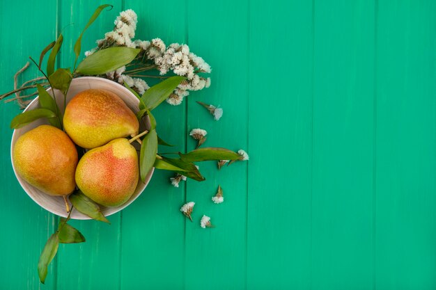 Top view of peaches in bowl with flowers on green surface