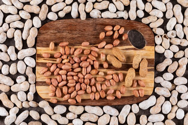 Top view peanuts on wooden cutting board surrounded by raw peanuts