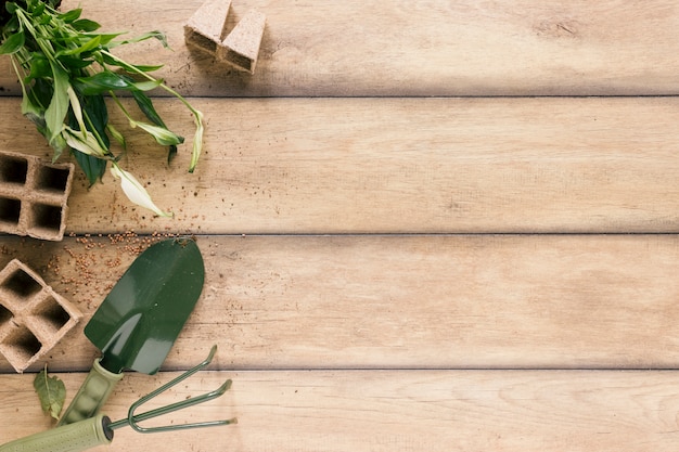 Free photo top view of peat tray; plant; showel and rake on wooden desk