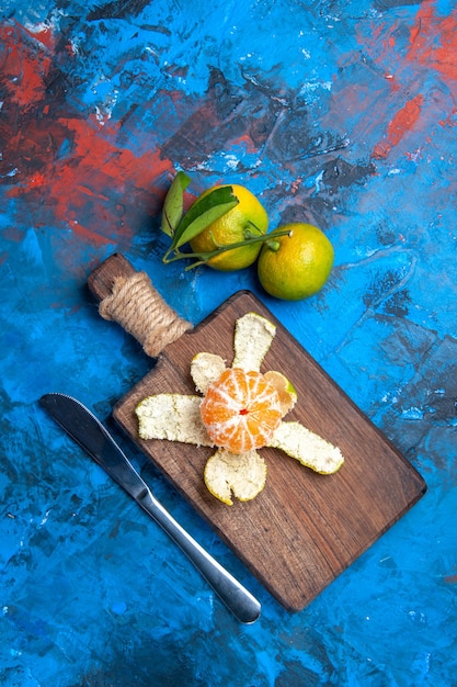 Free photo top view peeled mandarin on cutting board dinner knife fresh mandarines with leaves on blue surface free place