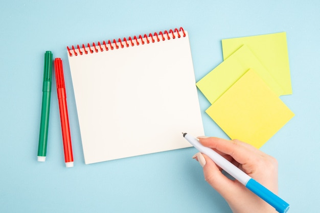 Top view pen in hand yellow sticky papers markers notepad on blue