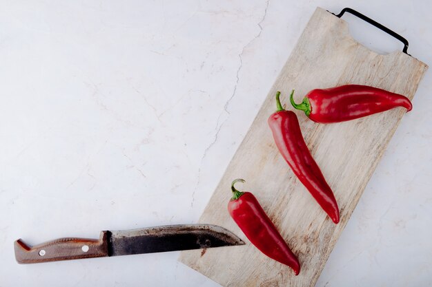 Top view of peppers on cutting board with knife on white background with copy space