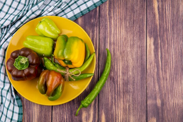 Free photo top view of peppers in plate with plaid cloth on wooden surface