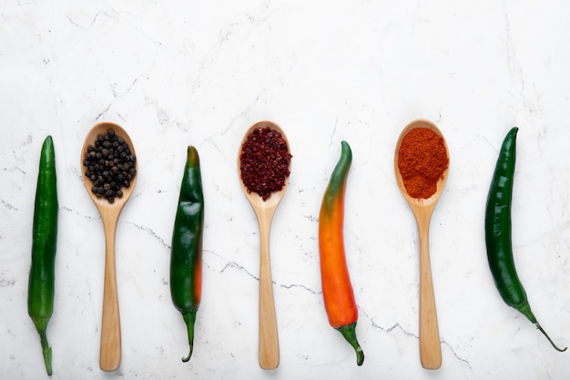 Top view of peppers and spoons full of spices on white background