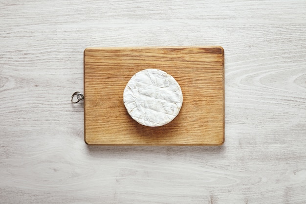 Free photo top view of perfect circle of camembert cheese on rustic wooden board isolated on aged white wooden table in center