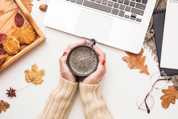 Free photo top view of person holding coffee with laptop and autumn leaves