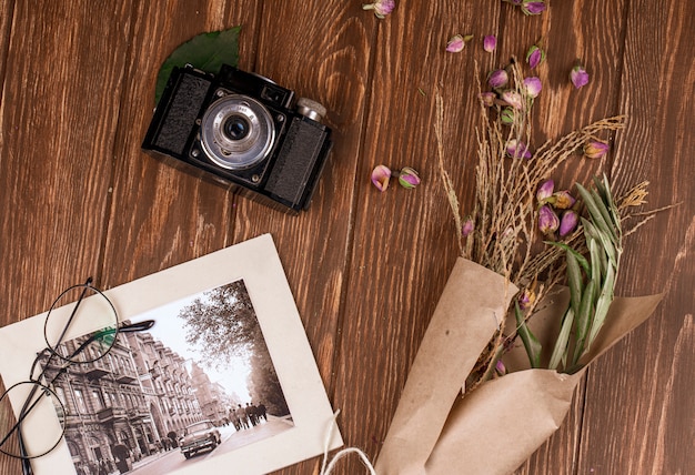 Free photo top view of photo and glasses old camera with white color dry branches in craft paper and dry rose buds scattered on wood