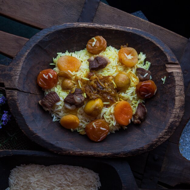 Top view pilaf with meet and dried fruits and chestnut and rice and rosemary leaves in wooden plate