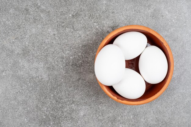 Top view of pile of eggs in potter bowl over grey table.