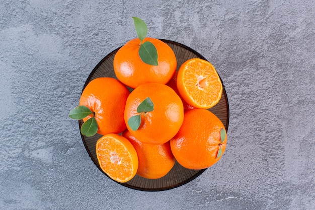 Top view of pile of tangerines in bowl over grey.