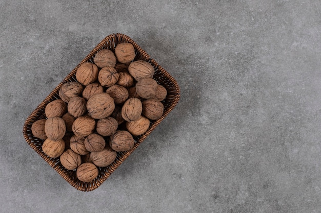 Free photo top view of pile of walnuts in basket over grey table.