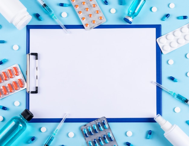 Top view pills spray, pill bottle, needles and paper holder in center on light cyan background. horizontal space for text