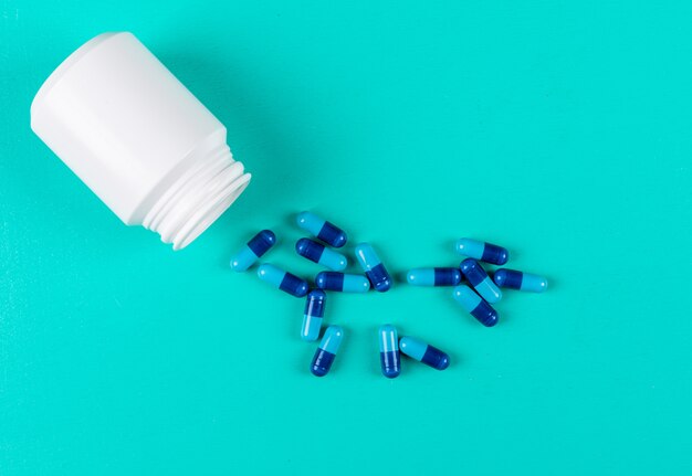 Top view pills with open pill bottle on cyan blue background. horizontal space for text