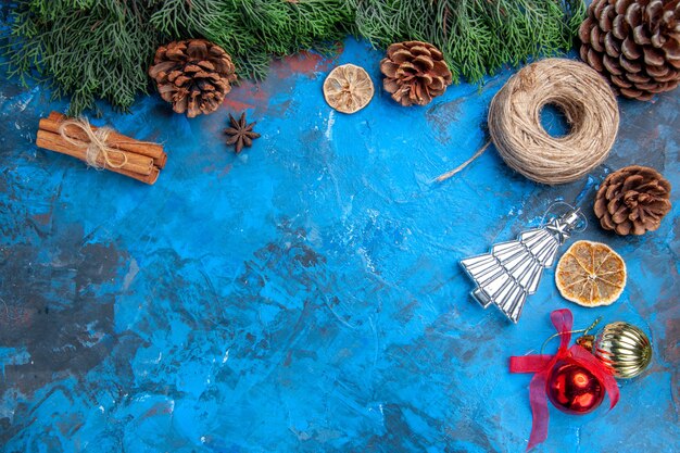 Top view pine tree braches straw thread cinnamon sticks dried lemon slices xmas tree toys on blue-red surface