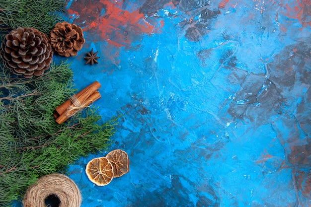 Free photo top view pine tree branches cones straw thread cinnamon sticks anise seed dried lemon slices on blue-red surface