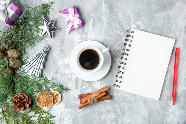 Top view pine tree branches notebook red pencil cup of tea cinnamon stick pinecones small gifts on grey surface