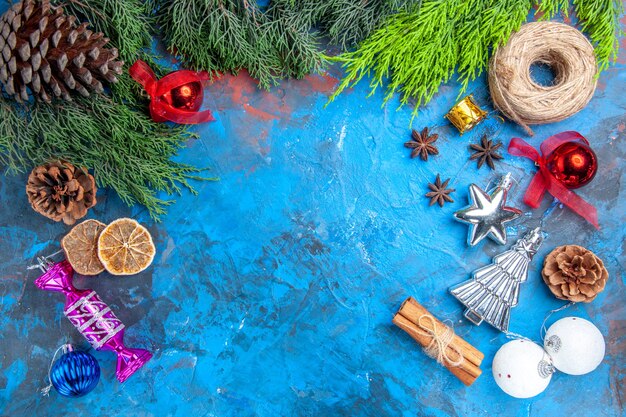 Top view pine tree branches pinecones straw thread xmas tree toys anise seeds cinnamon sticks dried lemon slices on blue-red background