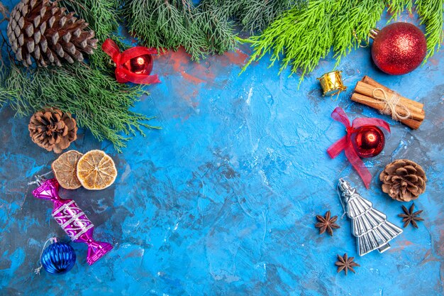 Top view pine tree branches pinecones xmas tree toys anise seeds dried lemon slices on blue-red background