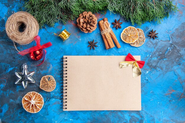 Top view pine tree branches straw thread cinnamon sticks dried lemon slices anise seeds a notebook on blue-red surface