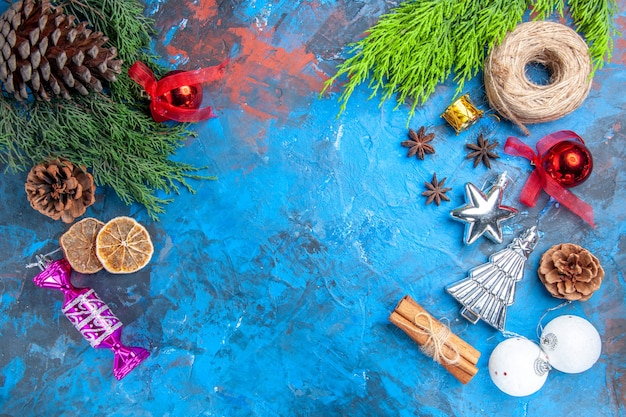 Top view pine tree branches straw thread xmas tree toys anise seeds cinnamon sticks dried lemon slices on blue-red background with copy place