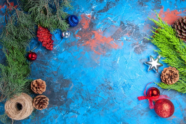 Free Photo top view pine tree branches with pinecones and colorful xmas tree toys straw thread on blue-red surface