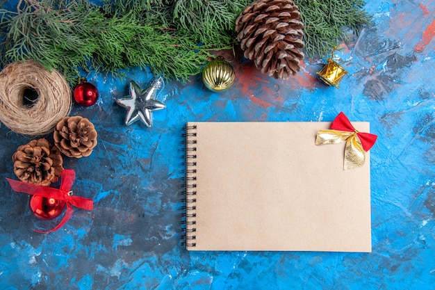 Top view pine tree branches with pinecones straw thread a notebook xmas tree toys on blue-red surface