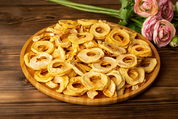 A top view pineapple dried rings inside desk dried fruits unique taste along with pink flowers on the brown wooden desk fruits exotic dry