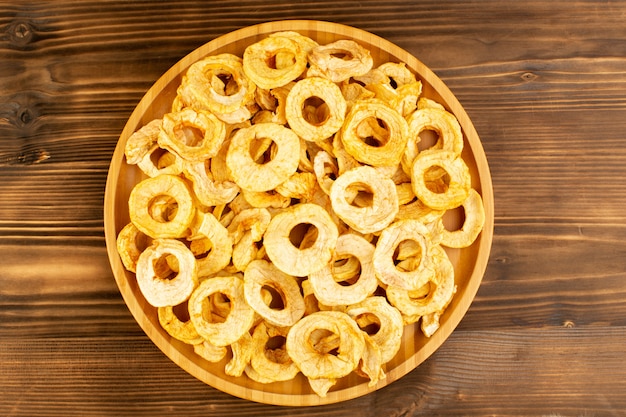 A top view pineapple dried rings inside plate dried fruits sour tasty unique taste on the brown wooden desk fruits exotic dry