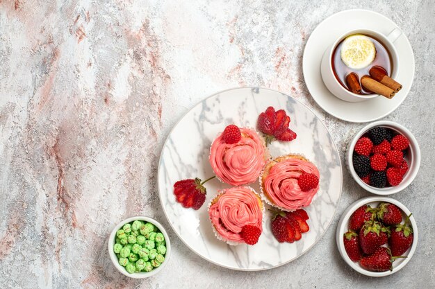 Top view of pink strawberry cakes with confitures and cup of tea on white surface