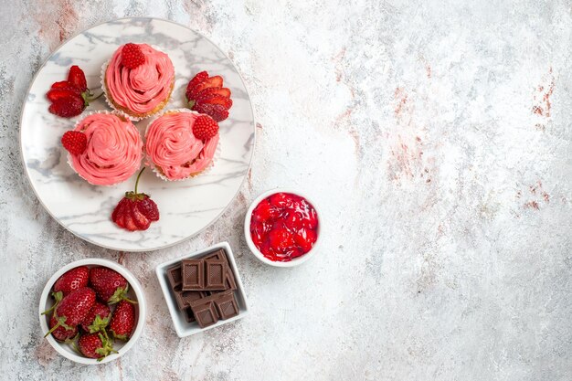 Top view of pink strawberry cakes with jam on white surface