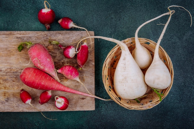 Free photo top view of pinkish red root vegetable beetroots on a wooden kitchen board with radishes with white beetroots on a bucket on a green background