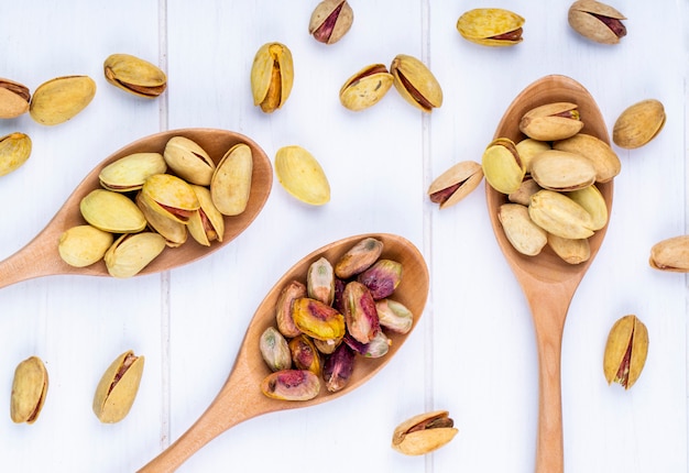 Top view of pistachio nuts in wooden spoons on white background