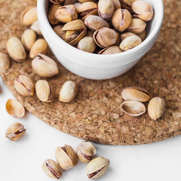 Top view of pistachio shells in white bowl on cork coaster