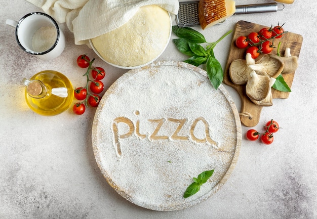 Free photo top view of pizza dough with mushrooms and tomatoes and word written in flour