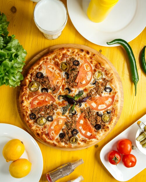 Top view of pizza with minced meat tomatoes and olives on a wooden plate