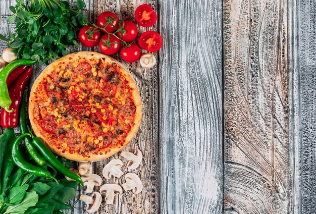 Top view pizza with peppers, mushrooms, tomatoes and grenery on light stucco background. vertical