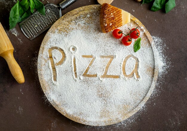 Top view of pizza written in flour with parmesan and tomatoes