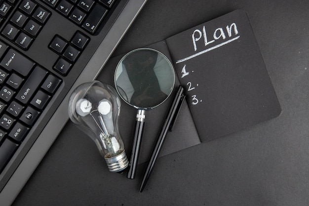 Top view plan written on black notepad lupa keyboard light bulb pen on black table