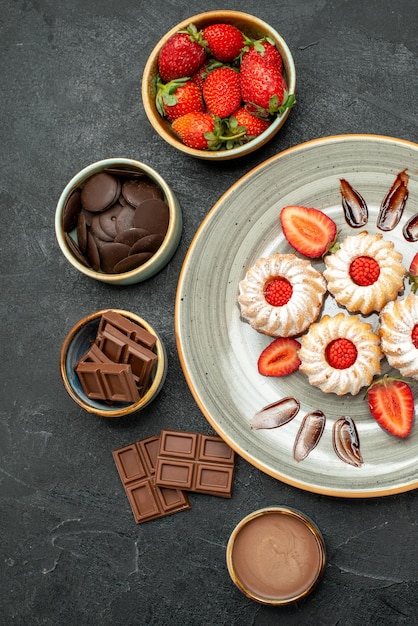 Top view plate of cookies plate of strawberry cookies with chocolate and bowls of chocolate strawberry and chocolate cream on dark surface