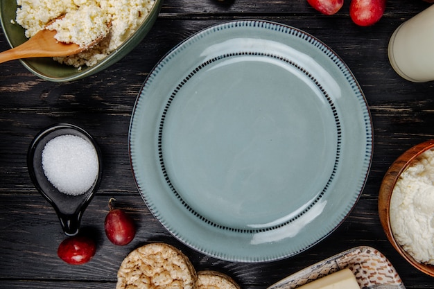 Free photo top view of a plate , cottage cheese in a bowl, fresh sweet grapes and sugar in a saucer on dark wooden table