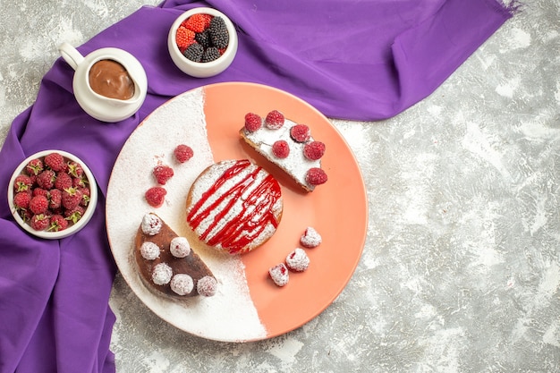 Free photo top view of plate of dessert on purple napkin with berries and chocolate on side on marble background