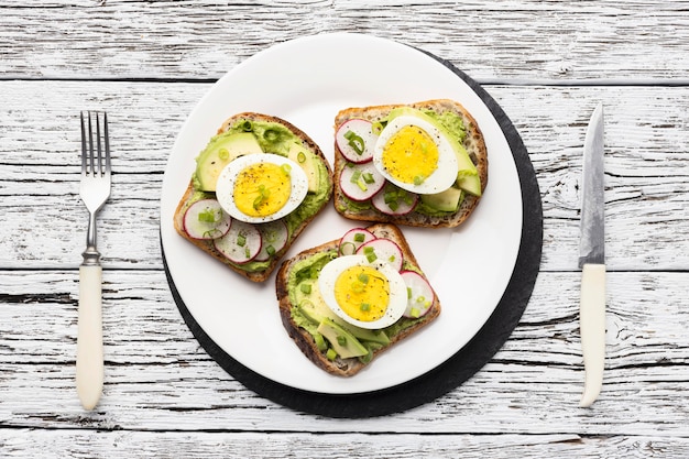 Top view of plate with egg and avocado sandwiches and cutlery