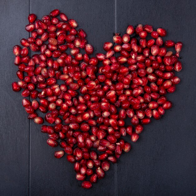 Top view of pomegranate berries on black surface heart concept